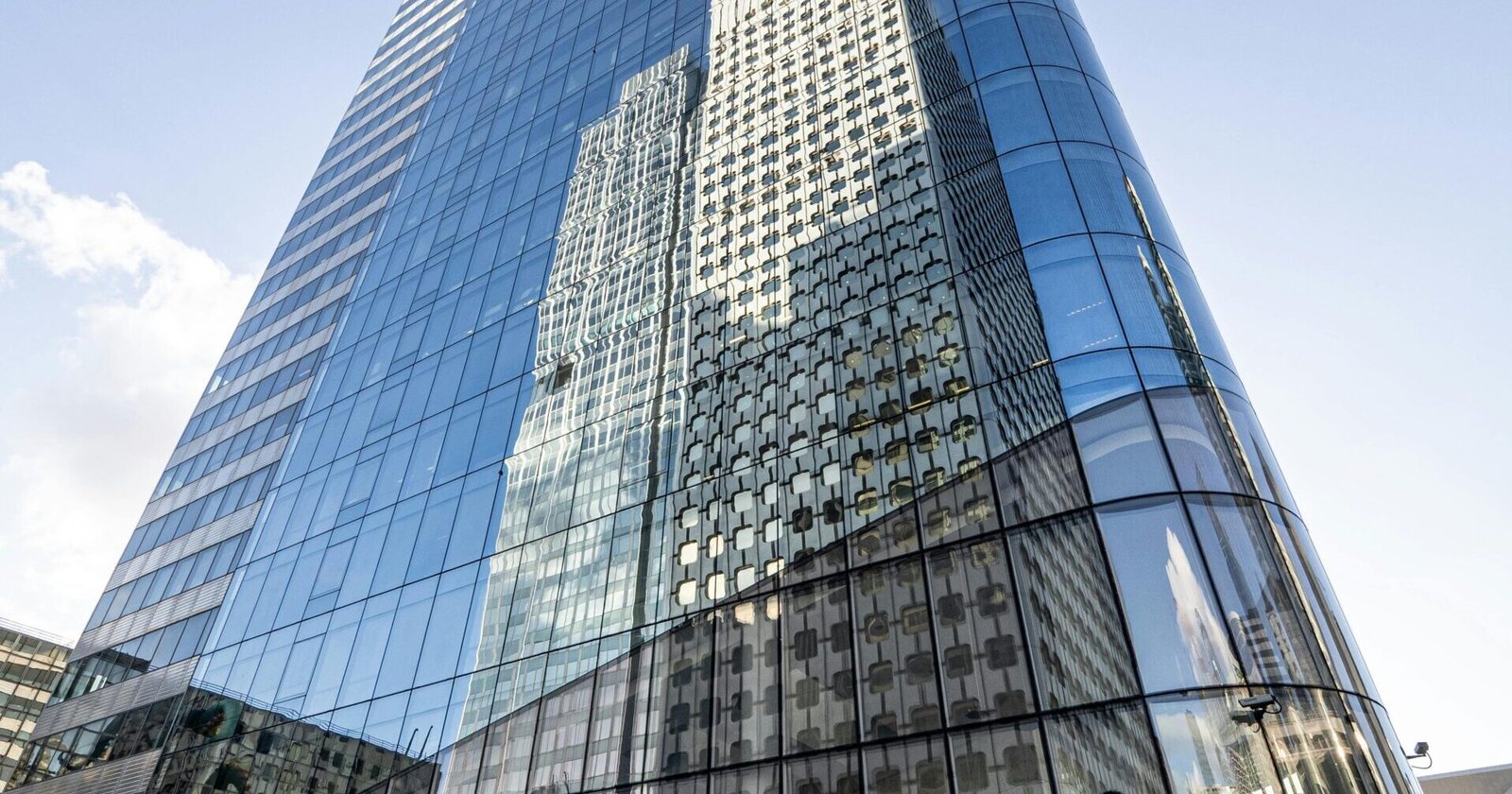 Contemporary glass skyscraper reflecting urban architecture in Paris's La Défense district on a clear day.