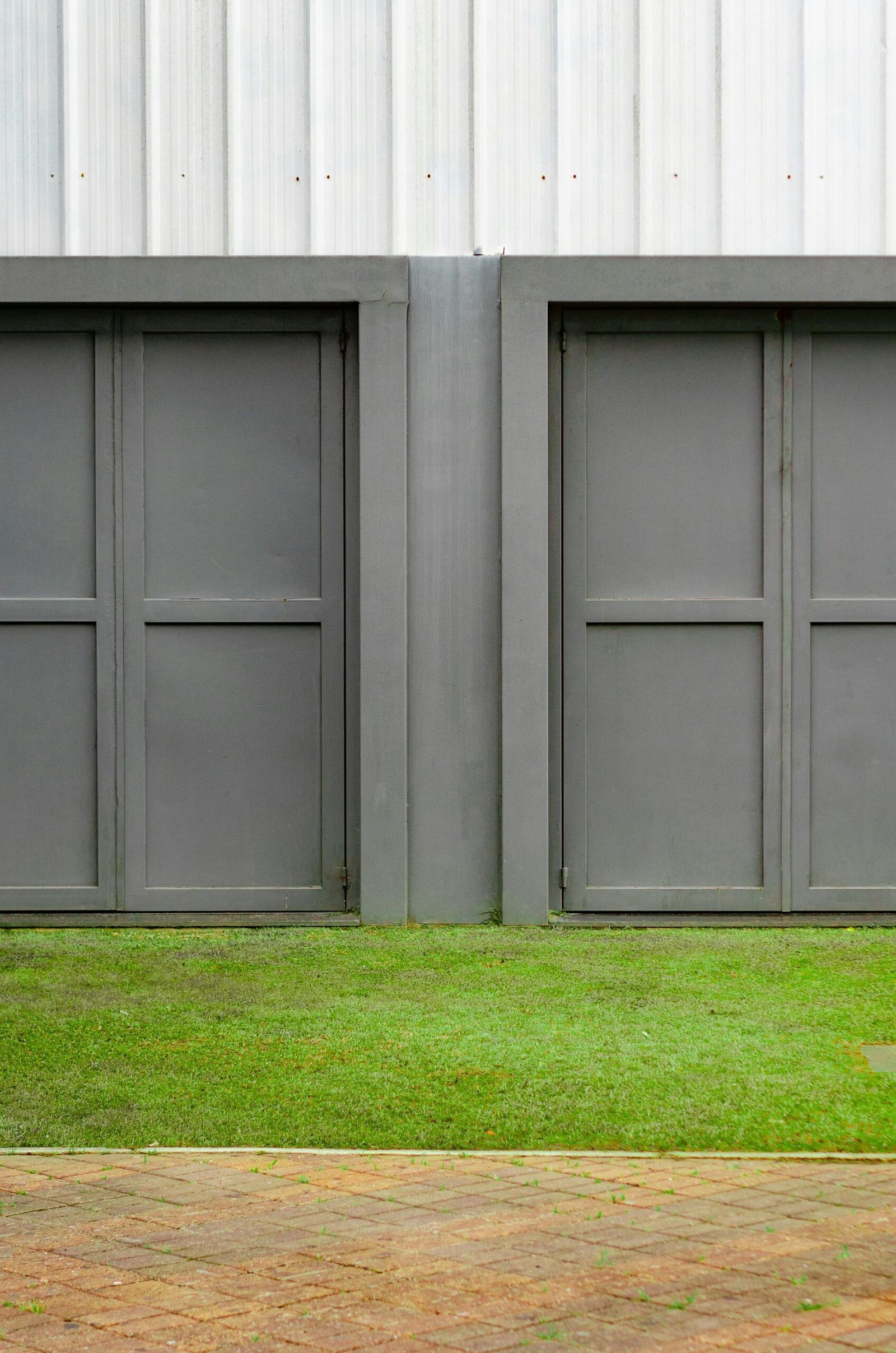 Close-up of two modern gray garage doors with grass and pavement.