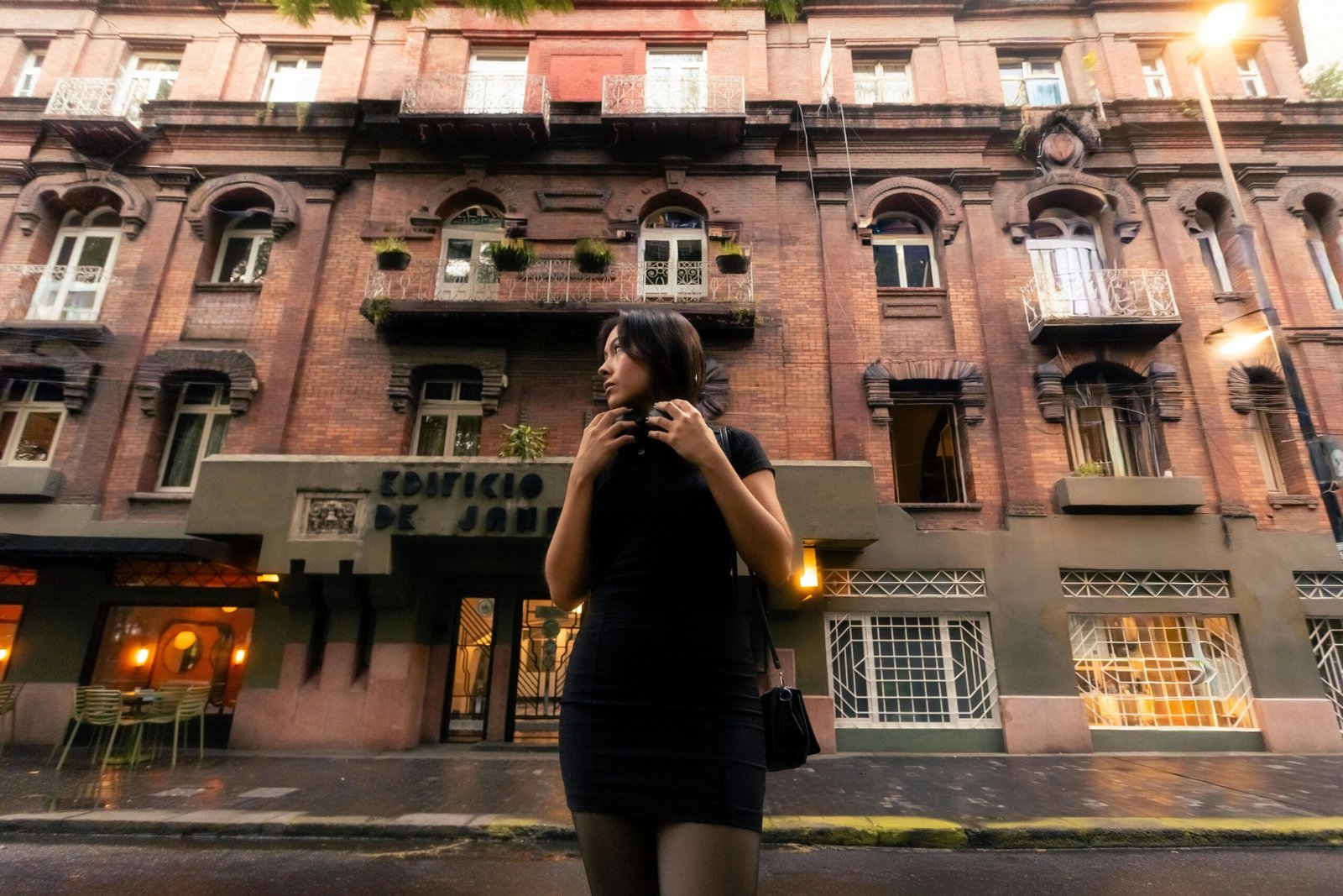 Young woman in black dress stands outside a historic building, exuding a classic and stylish vibe.